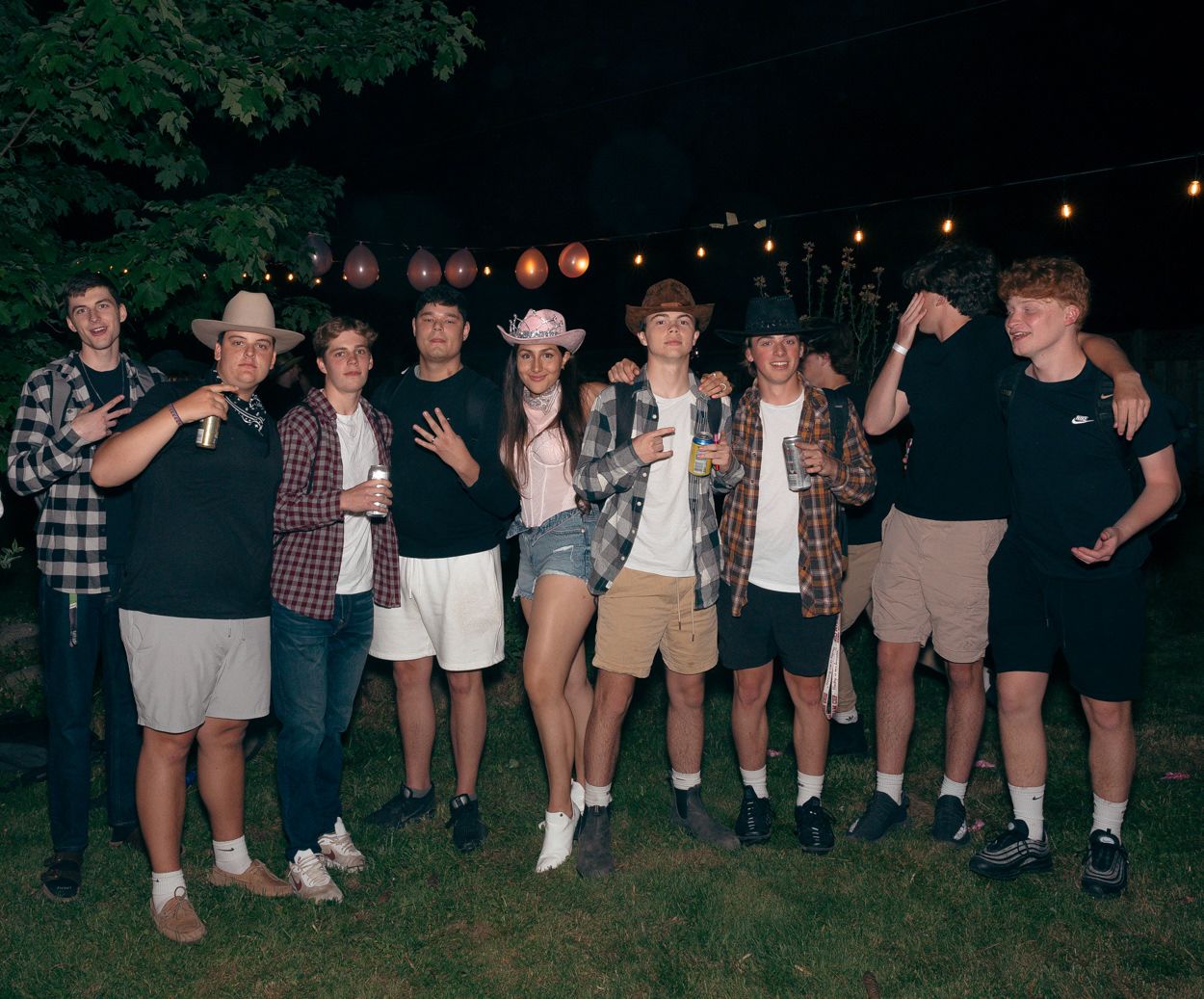 Large group of friends pose together at a nighttime outdoor party with string lights.