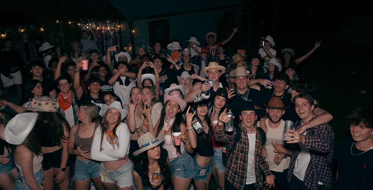 A crowd poses together wearing cowboy hats at a western-themed outdoor night party.