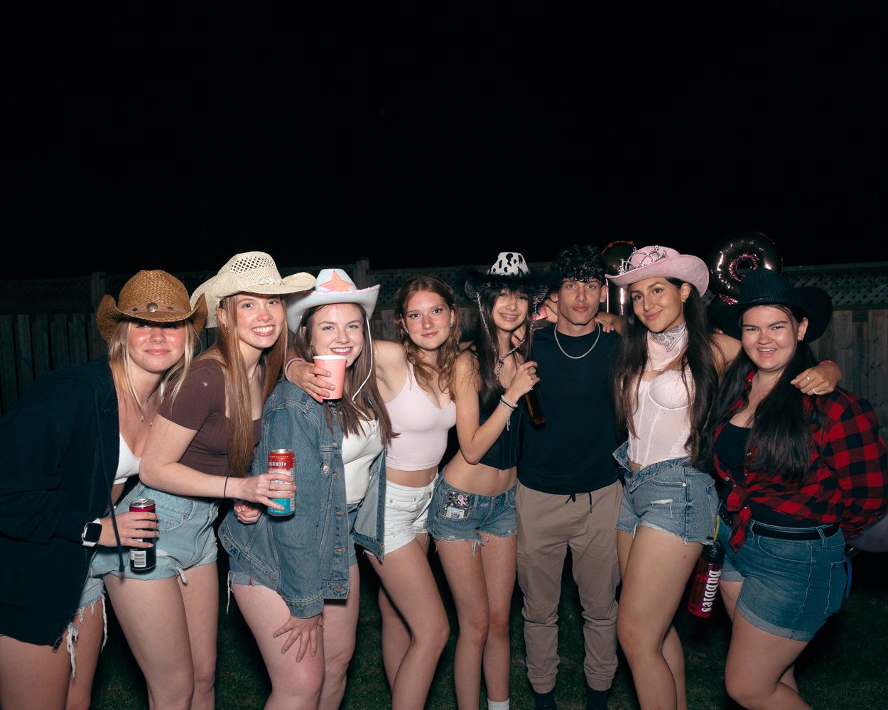 Friends in western-themed attire gather for a group photo at a nighttime party.