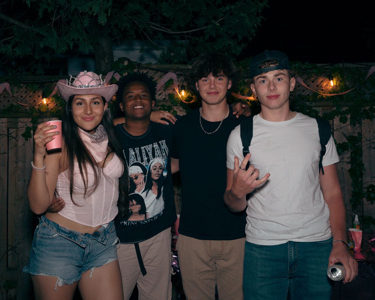Young people posing together at a casual outdoor gathering with string lights in the background.