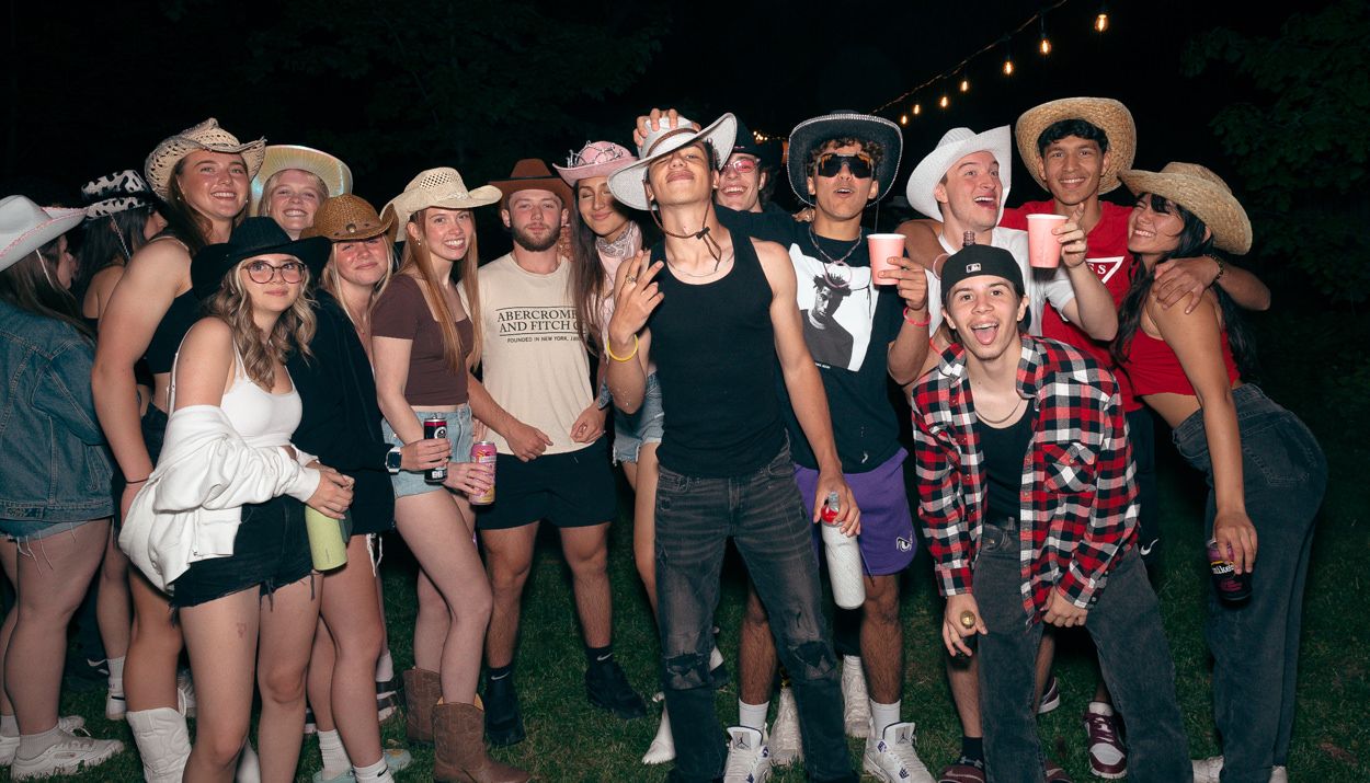 Large group wearing cowboy hats and casual attire poses together at a western-themed outdoor party.