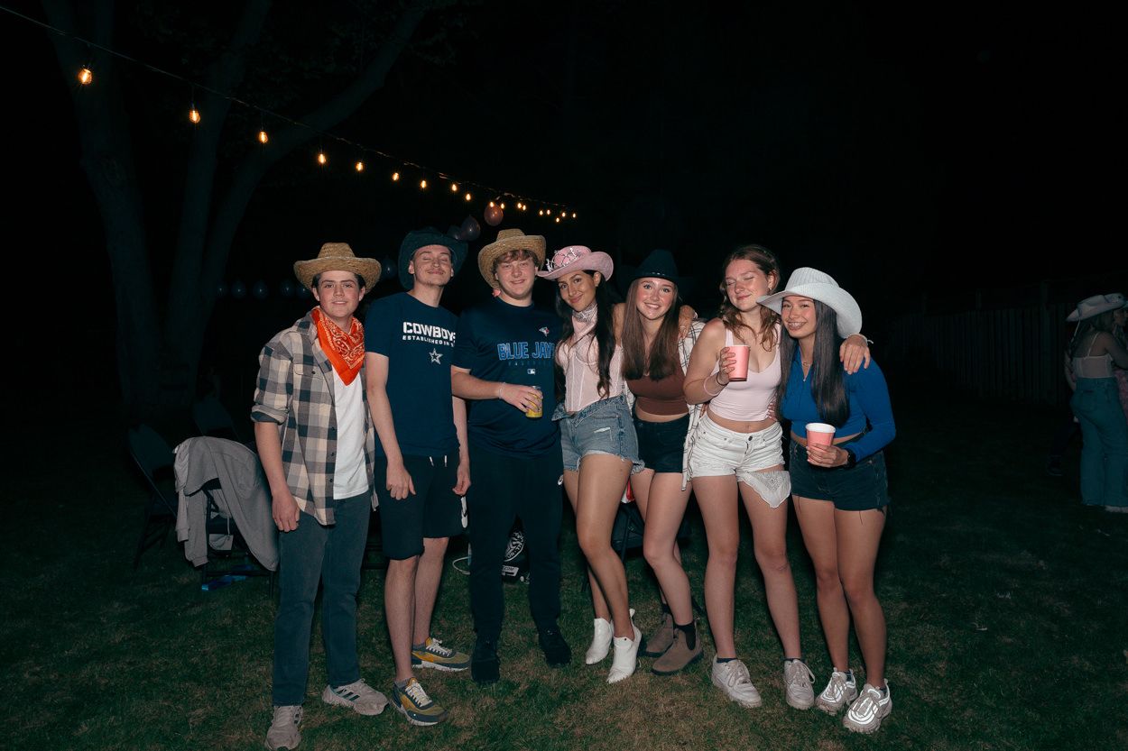 Group photo of friends at a western-themed outdoor party with string lights overhead.