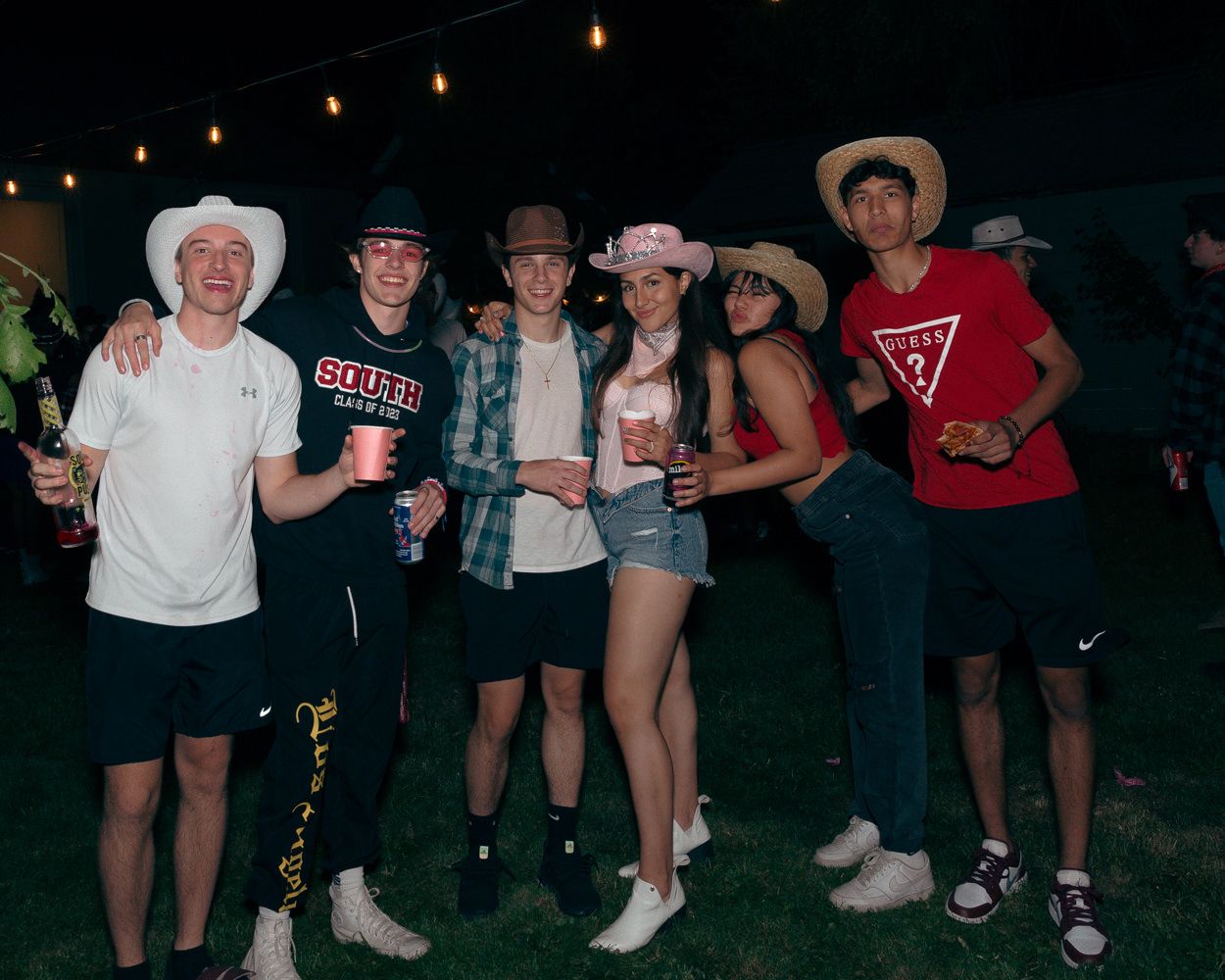 Friends in western wear and casual clothes gather under string lights at an outdoor party.