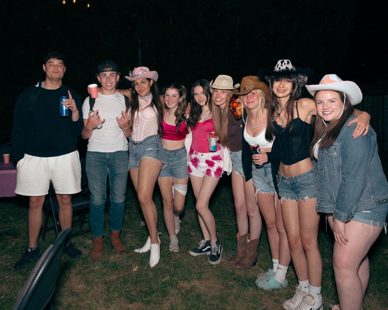 Group of friends in western-themed outfits pose together at an outdoor nighttime gathering.