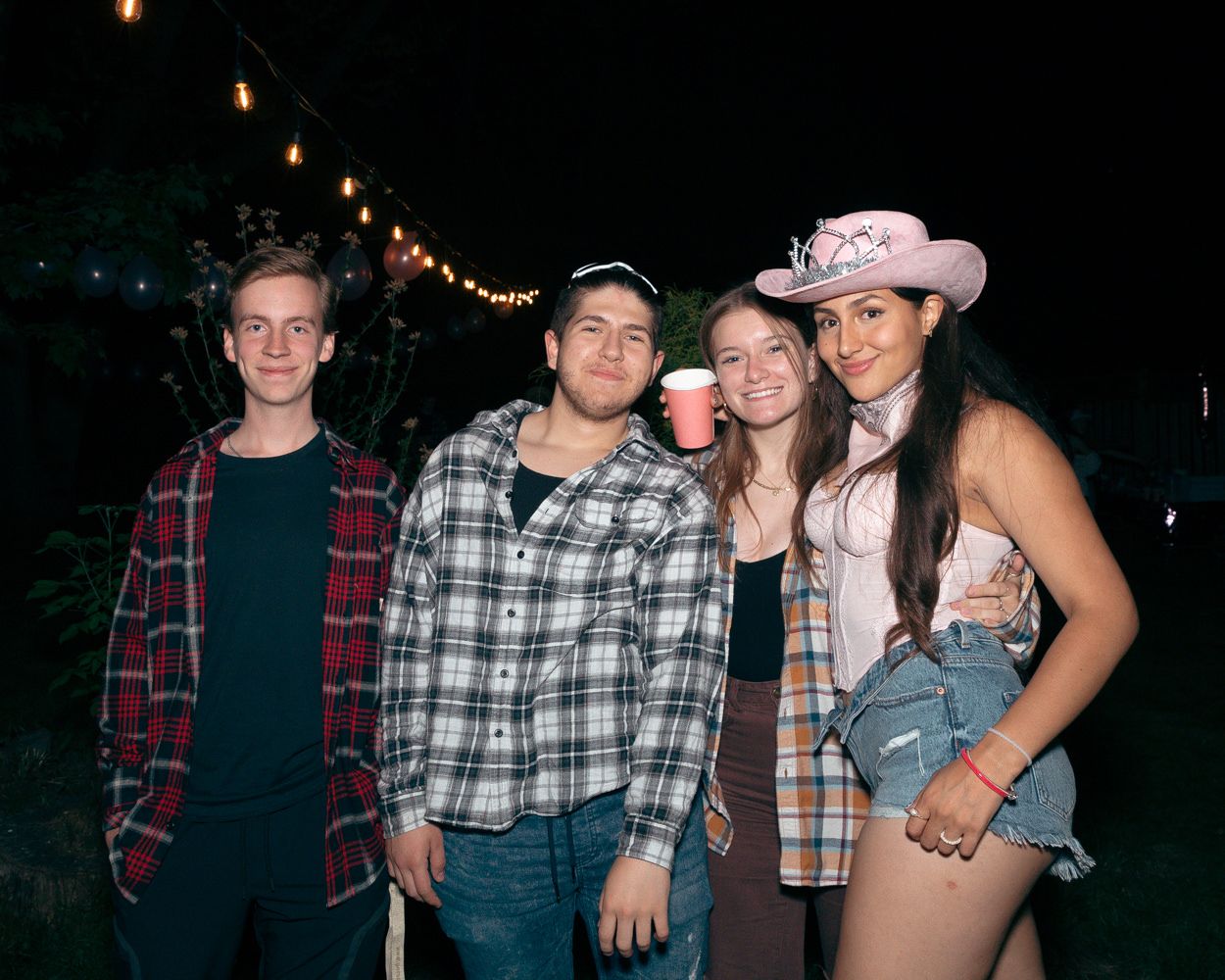 Four friends pose together at night wearing plaid shirts and western party attire.