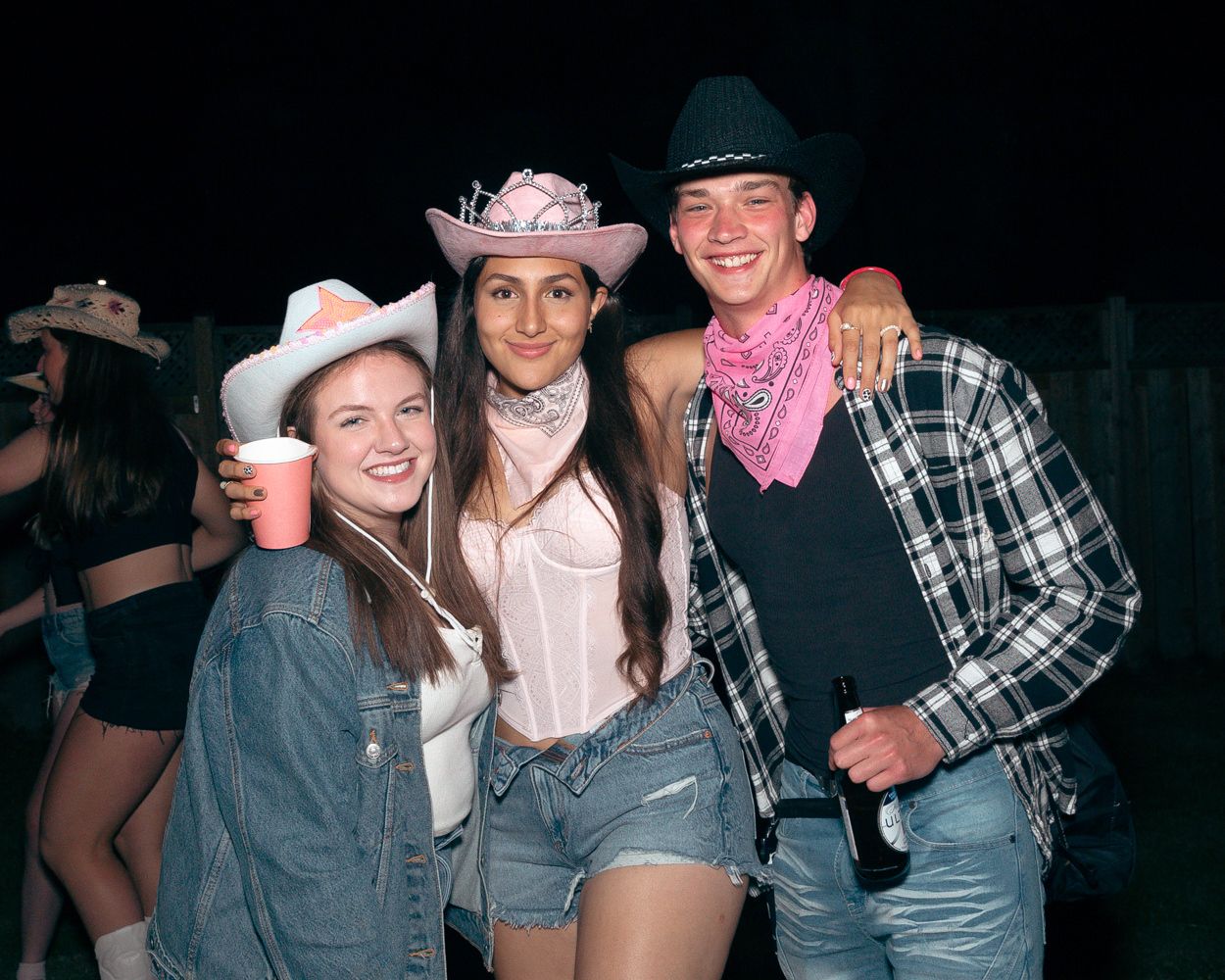Friends dressed in western-themed outfits with cowboy hats at an outdoor party.
