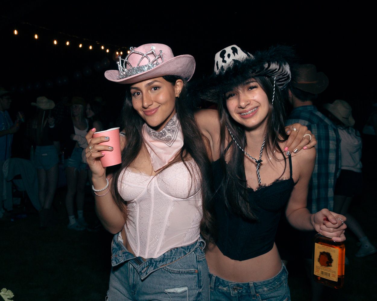 Two friends in western and halloween costumes pose with drinks at a nighttime party.