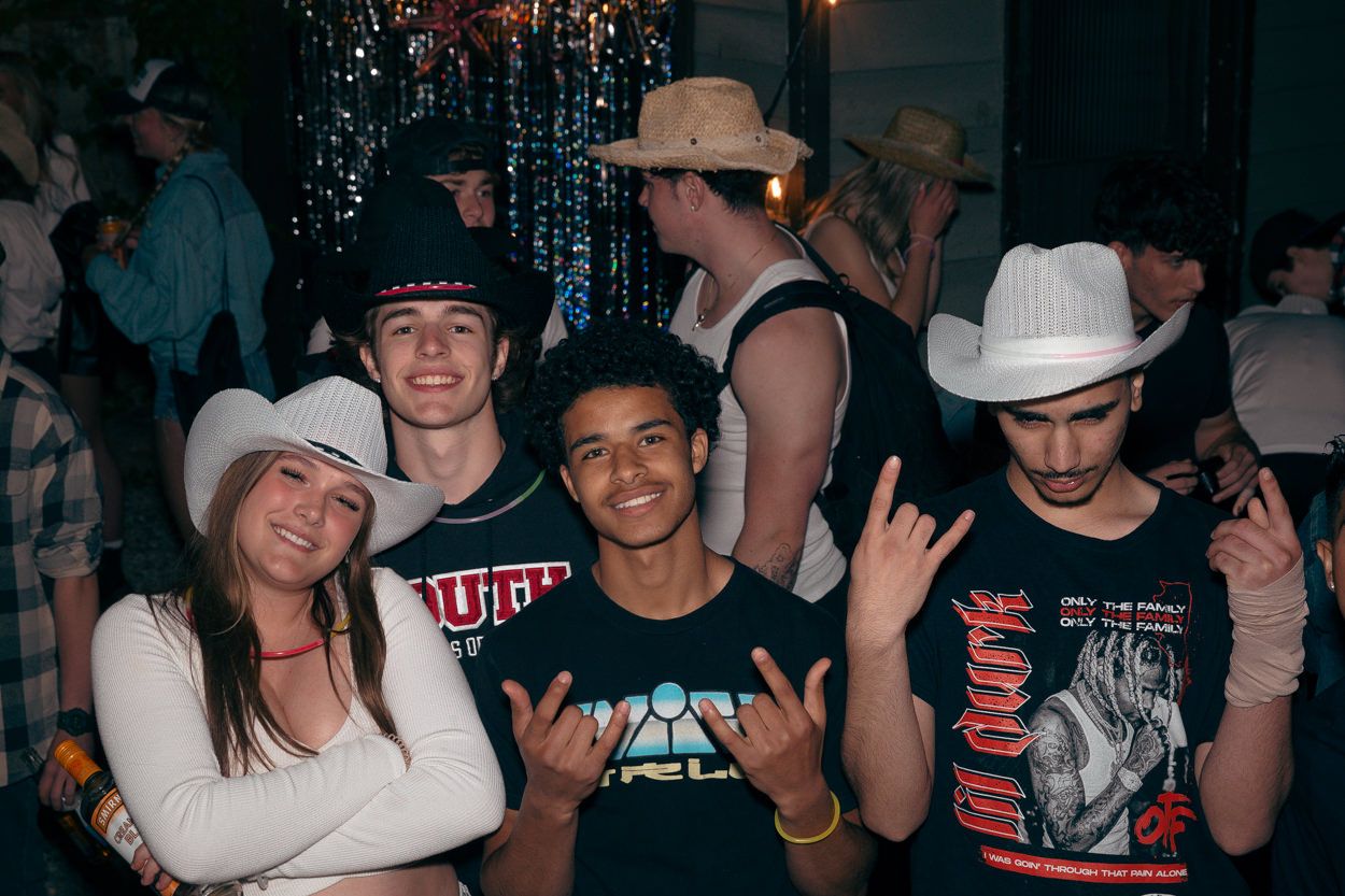 Group of partygoers in western hats and casual wear pose together indoors.