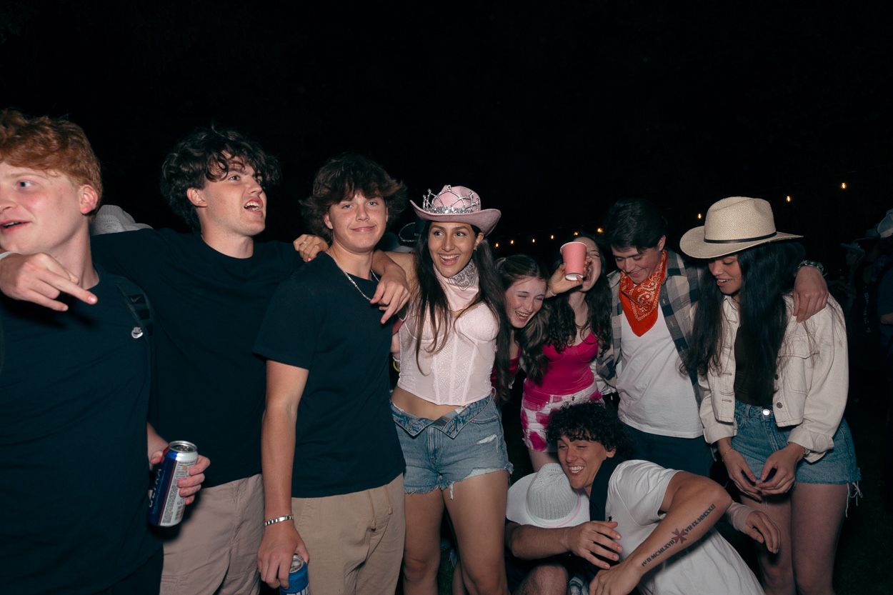 Party goers in casual summer clothes and cowboy hats gathered at a nighttime event.