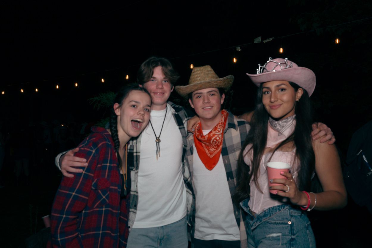 Four friends pose together at a nighttime outdoor party wearing western-themed attire and cowboy hats.