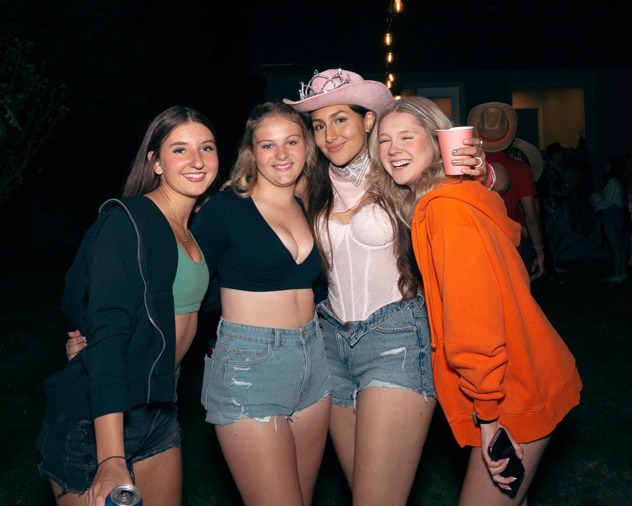 Group of friends in casual summer outfits enjoying a nighttime outdoor party with string lights.