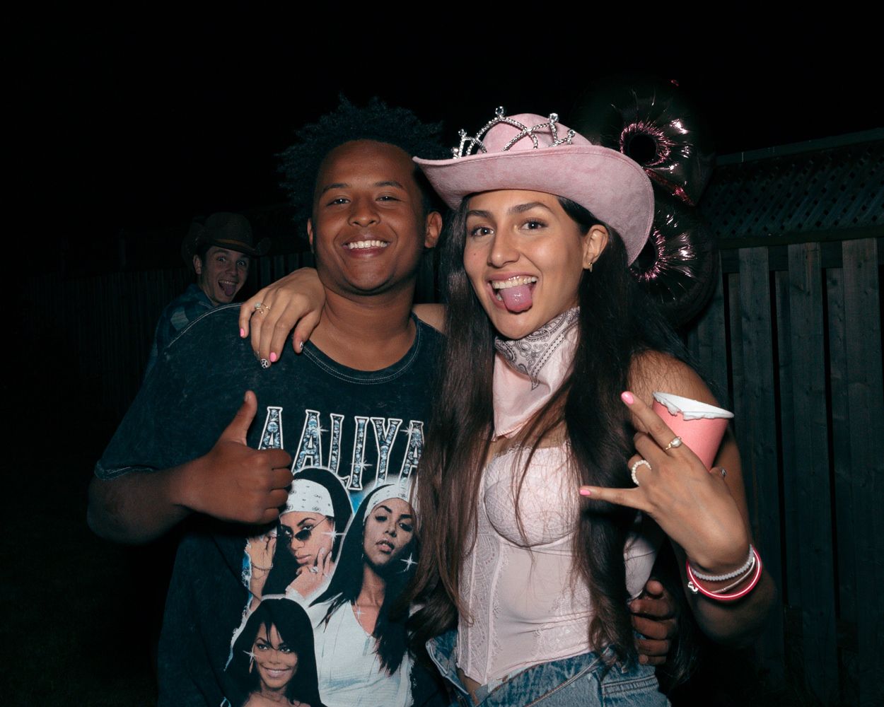 Friends pose together at a western-themed party wearing casual attire and cowboy accessories.