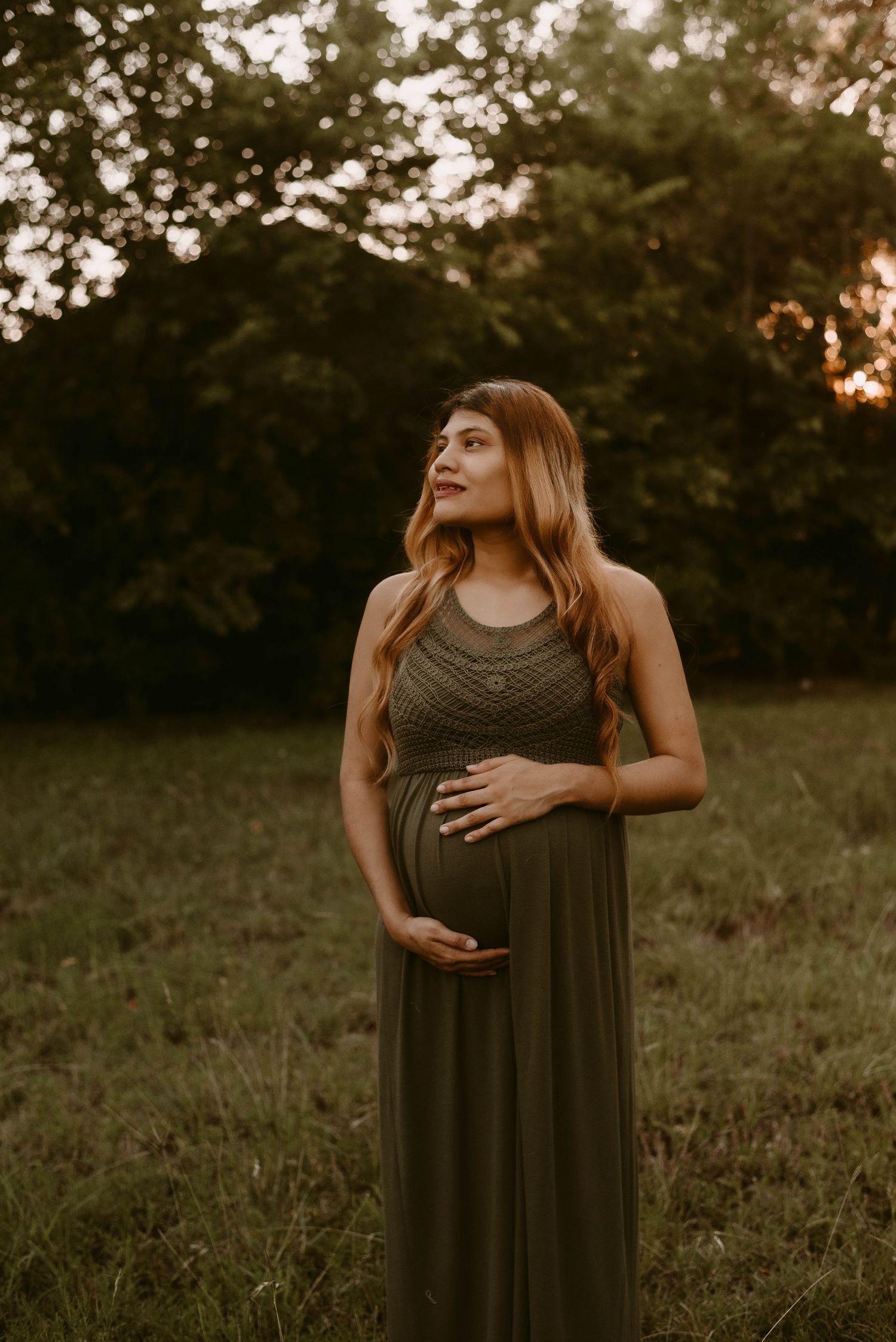 Elegant maternity portrait in olive dress with flowing hair during golden hour photography.
