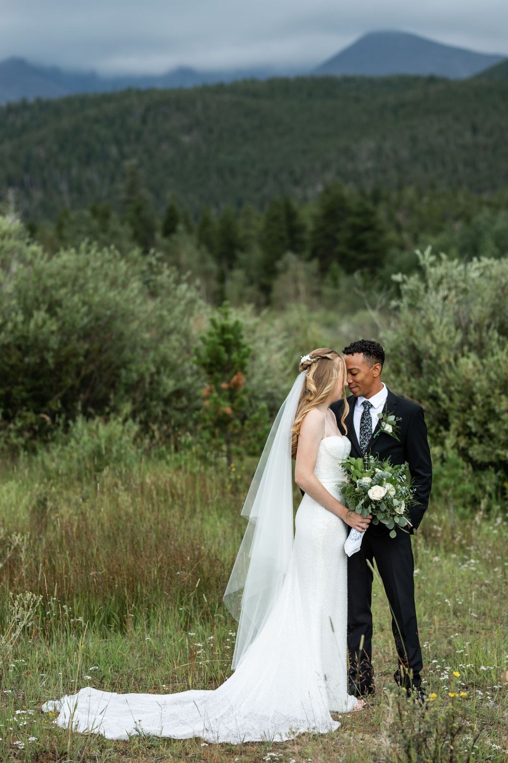 A romantic wedding portrait in a mountain meadow with evergreen forests in the background.