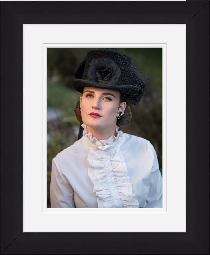 A vintage-inspired portrait showing a figure in a black hat and white ruffled blouse against a dark background.