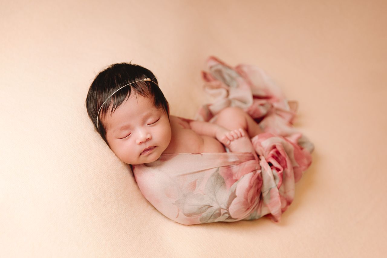 sleeping baby on peach blanket wrapped in floral scarf