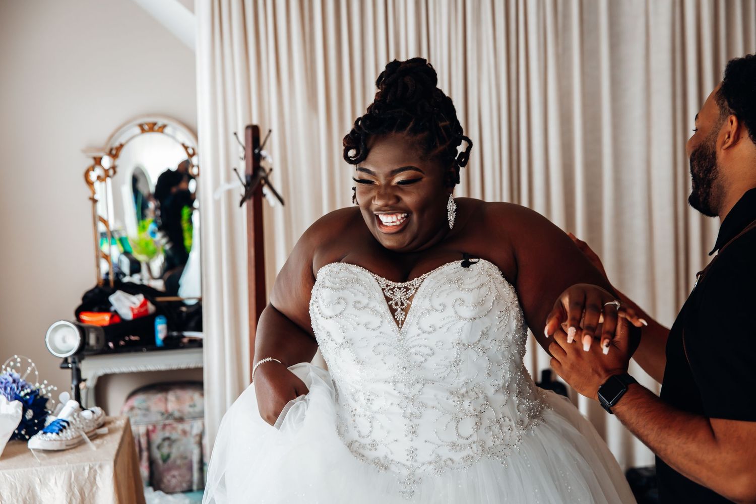 Joyful bride in strapless lace ball gown laughs while being helped getting ready on her wedding day.