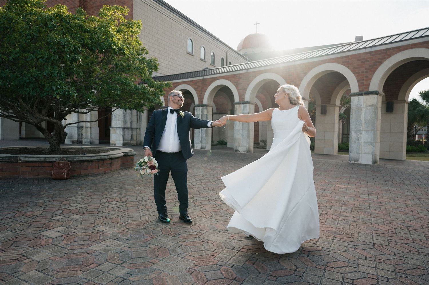 Wedding couple spins and dances under brick archways at sunset.