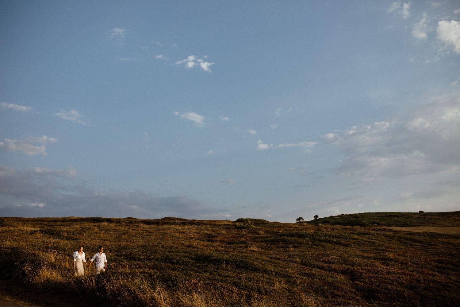 A scenic landscape at dusk with rolling brown hills and a bright blue sky dotted with wispy clouds. Wedding photographer in Mexico Riviera M