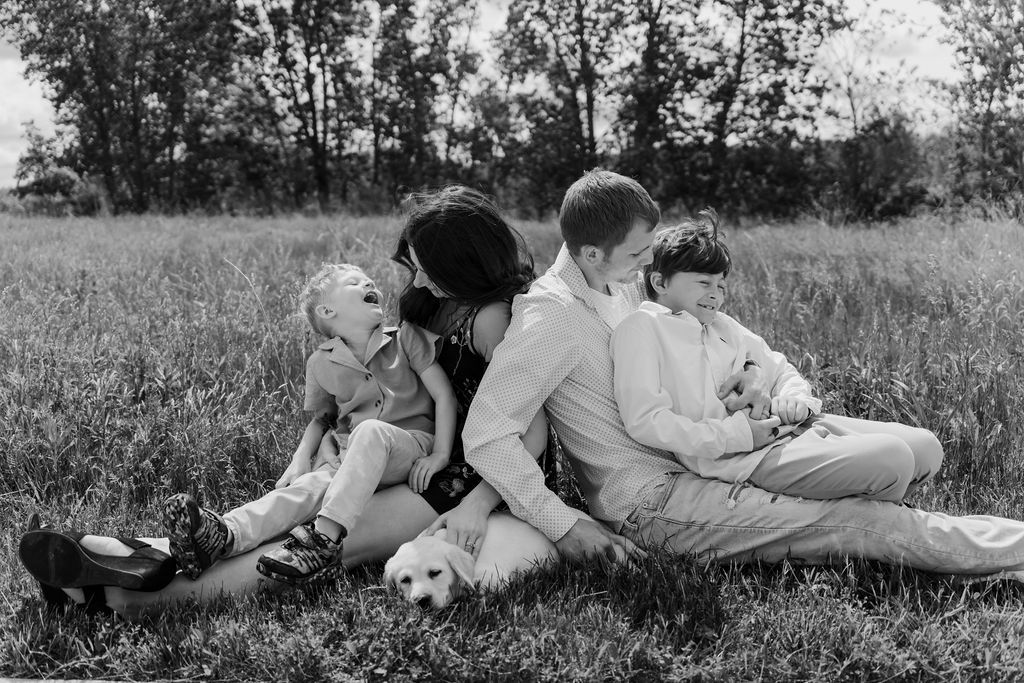 Happy family moment in a field with mom, dad, and two boys sitting together. Candid family photography