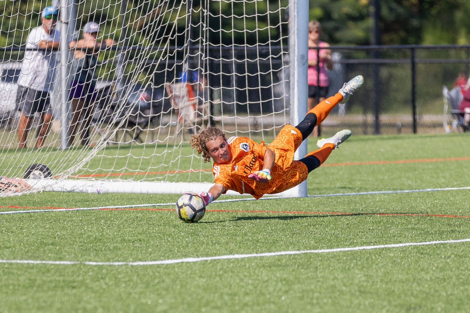 Soccer goalkeeper diving to make a save in front of goal net on grass field.