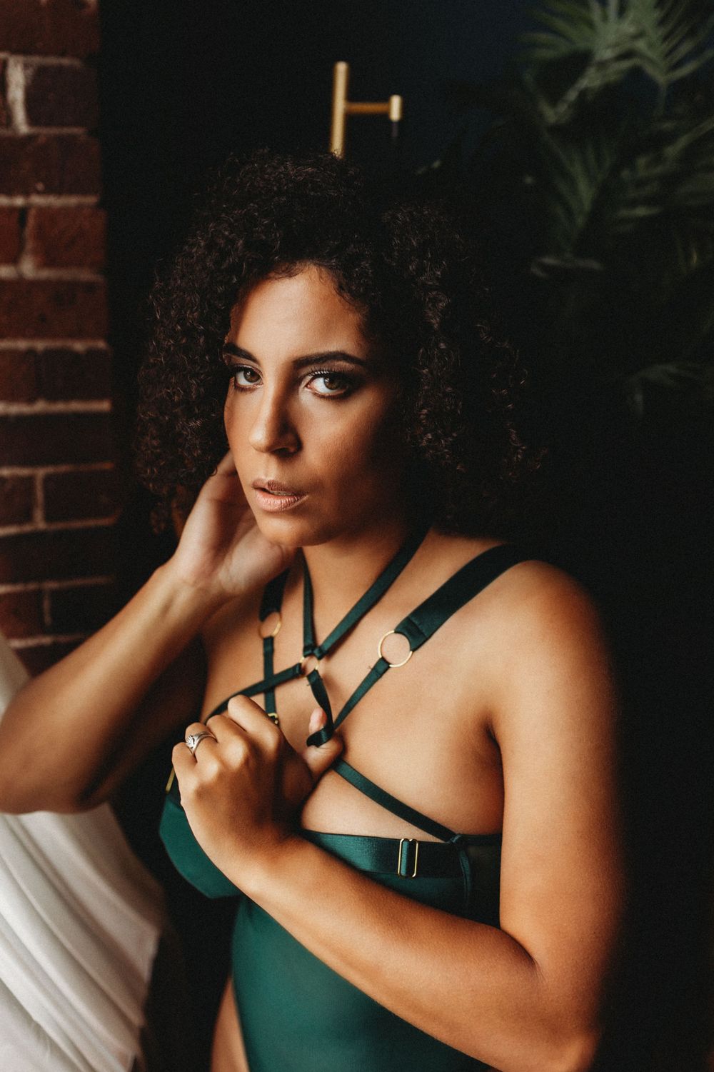 Portrait in emerald lingerie with harness details against brick wall.