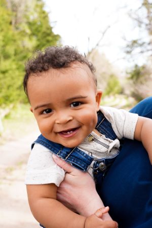 Baby wearing denim overalls smiles brightly during an outdoor photo session.