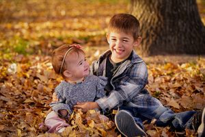 Two children sitting together and smiling in fallen autumn leaves.