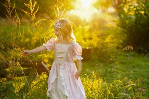 A child in a white dress twirls in a sunlit garden during golden hour.