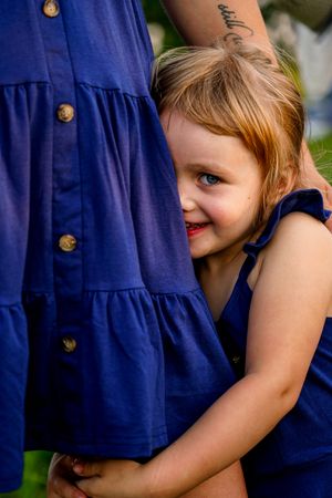 Young child in navy blue dress hugs adult wearing matching dress with gold buttons.