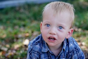 Close-up portrait of young child wearing denim shirt outdoors.