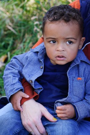 A toddler wearing a denim jacket and navy shirt sits outdoors in casual attire.