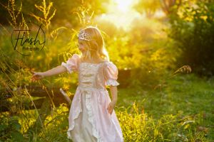 Child in white dress twirling in golden sunlit garden.