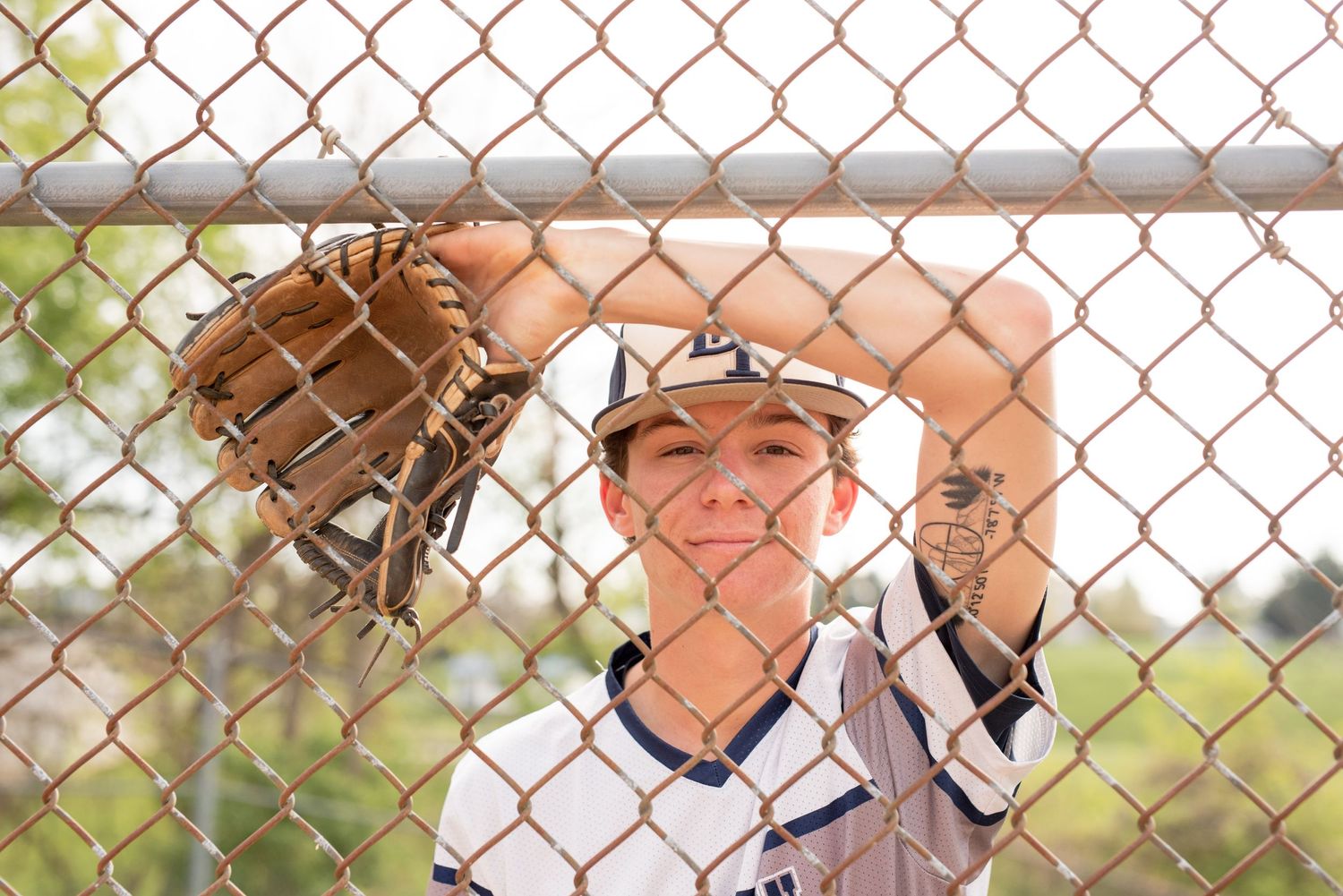 Baseball player with glove standing behind chainlink fence during practice.