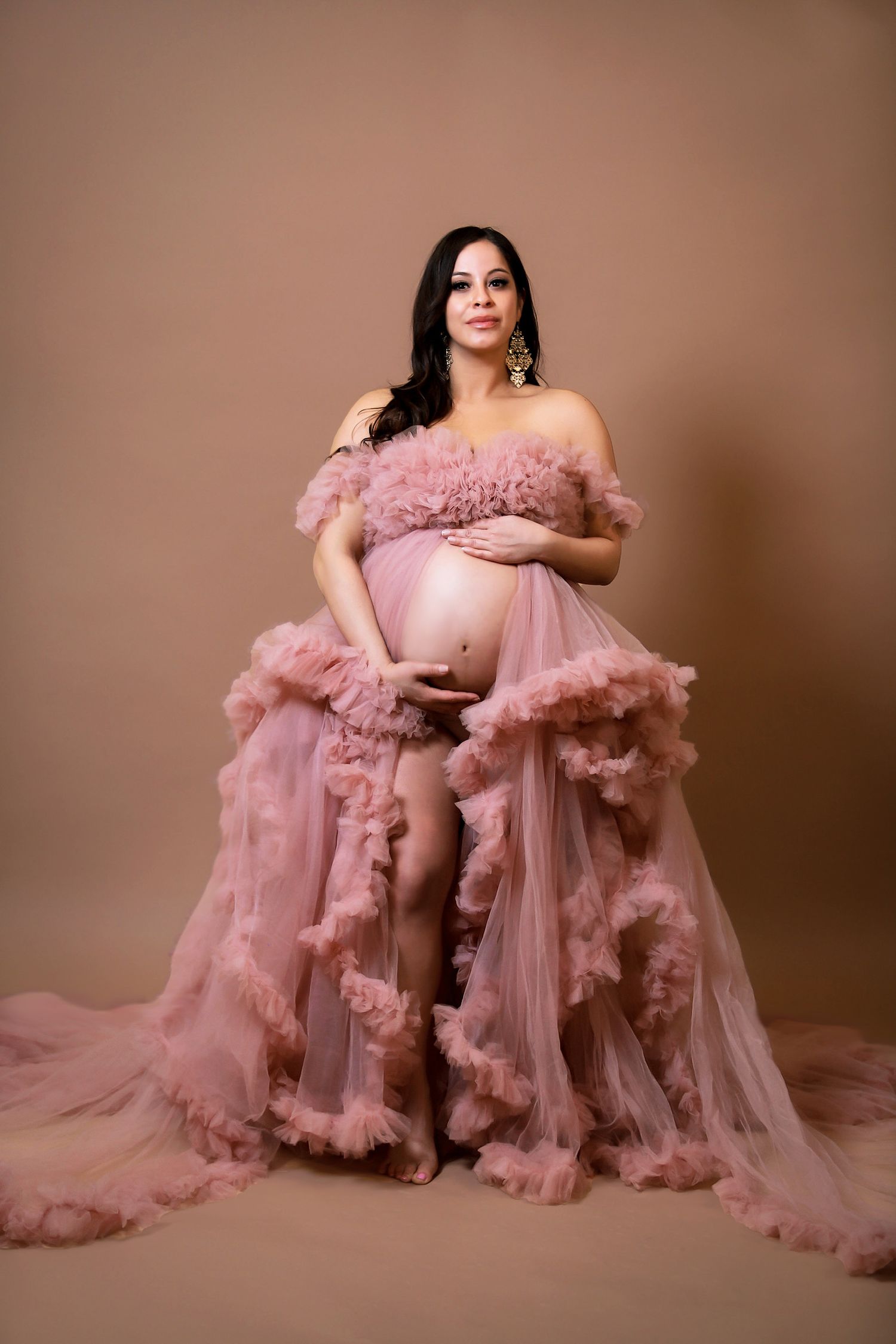 Maternity photos in flowing pink tulle gown showing elegant poses against warm backdrop.