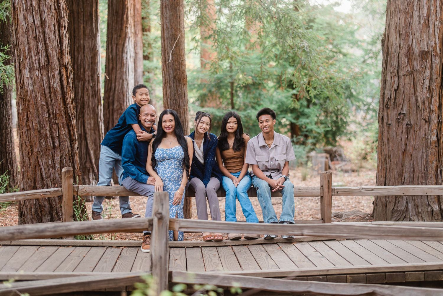 People sitting together on a wooden bench surrounded by towering redwood trees in a forest.