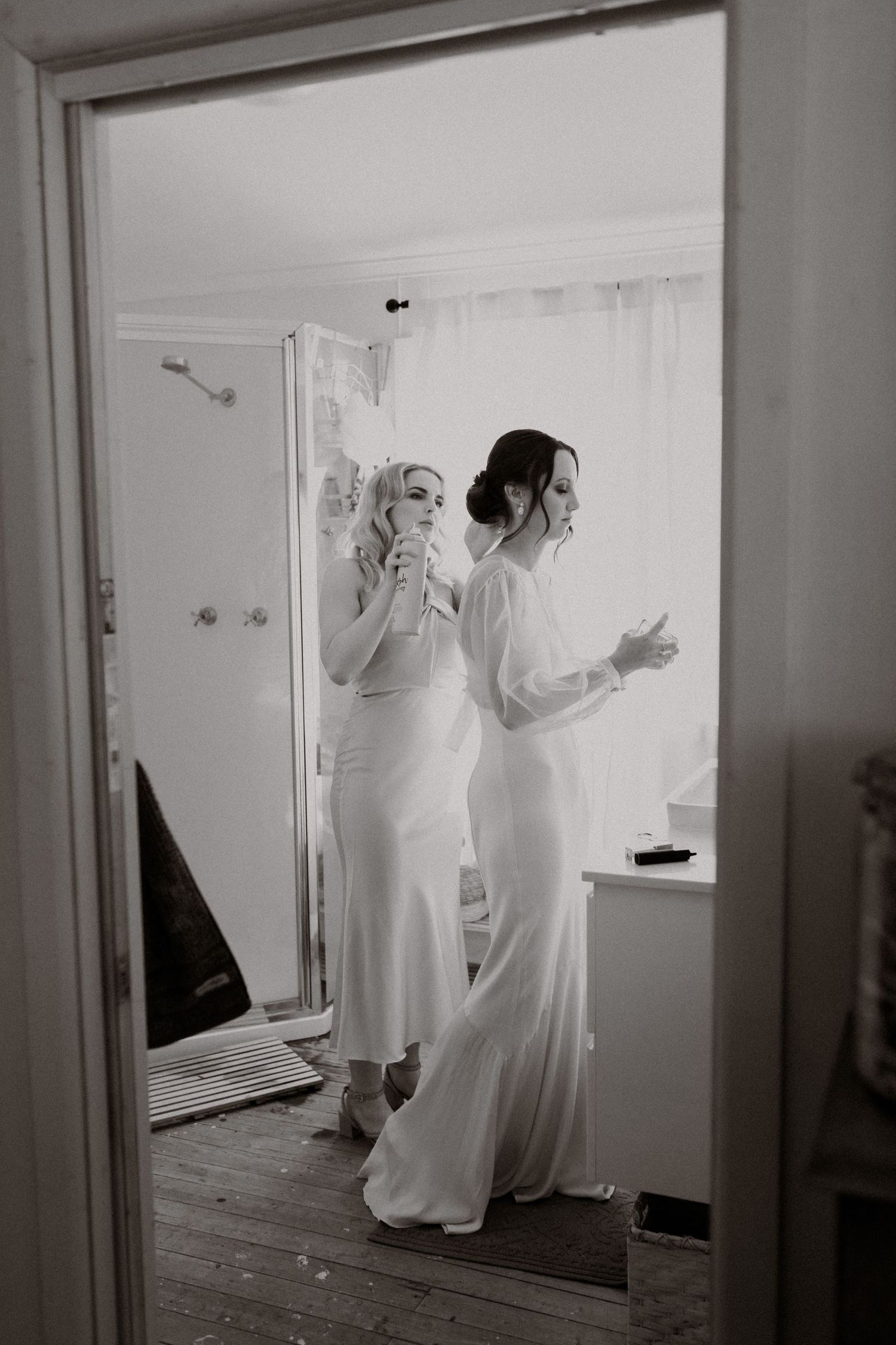 Two people in elegant white dresses getting ready in a bright room.