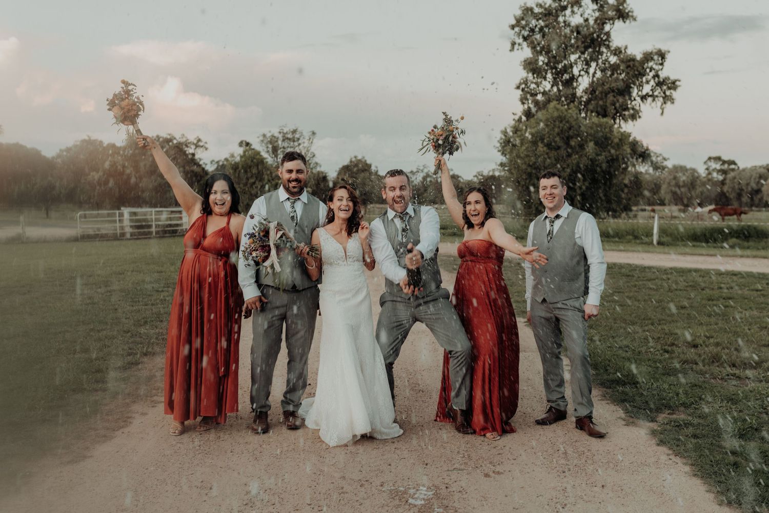Wedding party in red dresses and gray suits celebrating on a rural path.