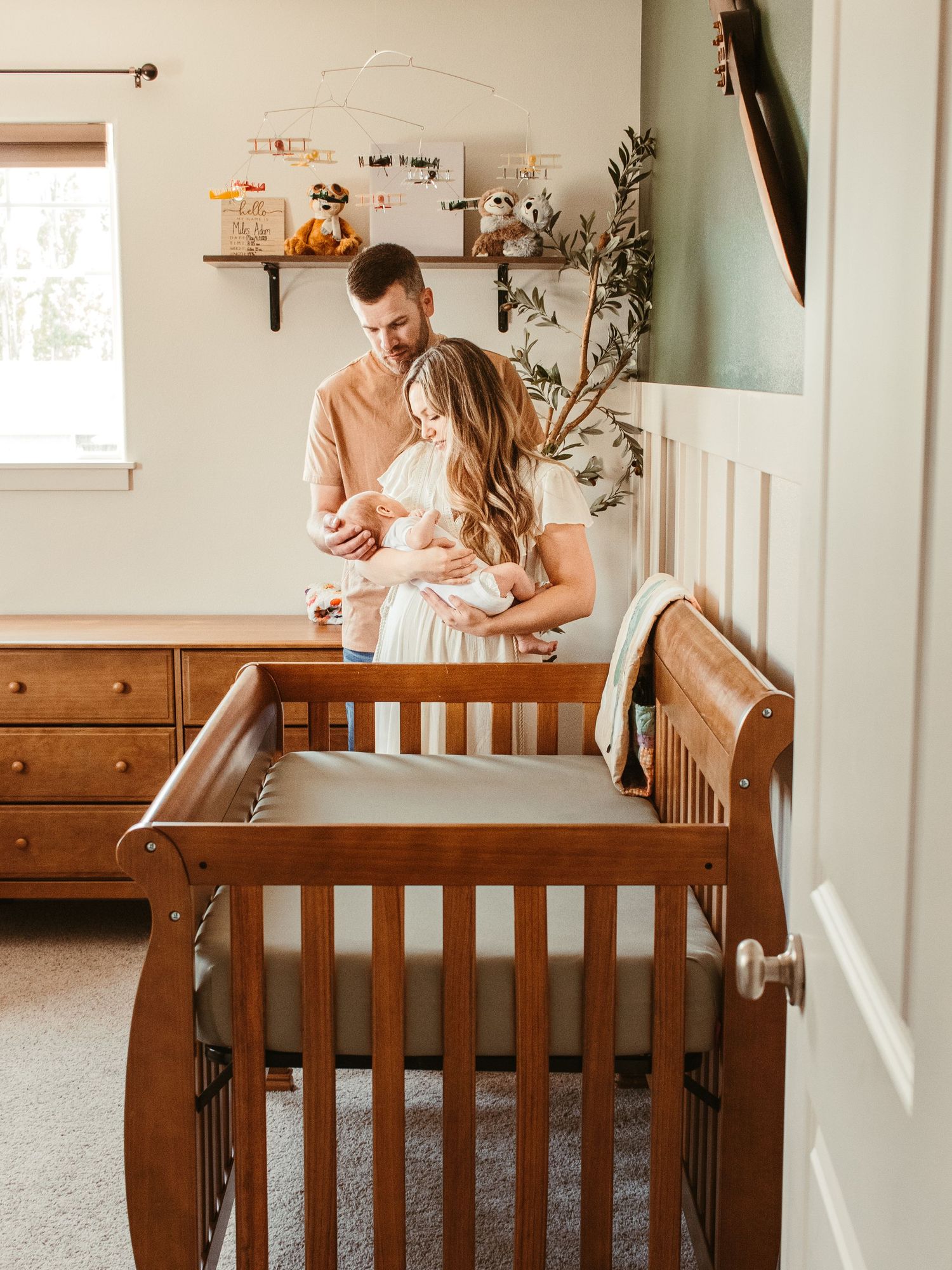 Interior nursery scene with wooden crib and couple admiring their baby.