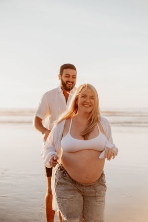 Joyful maternity photo session with couple laughing together on a sunny beach.