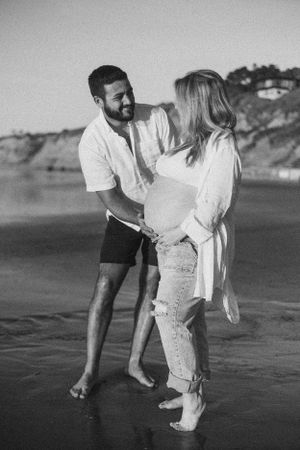Black and white beach portrait of expecting couple sharing intimate moment.