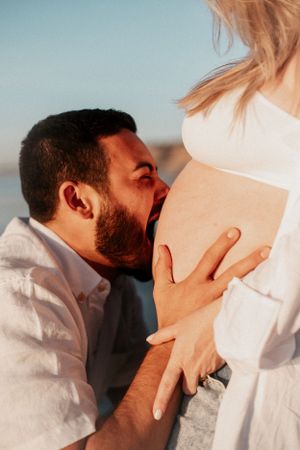Romantic beach maternity photoshoot showing an intimate moment between expectant parents at sunset.