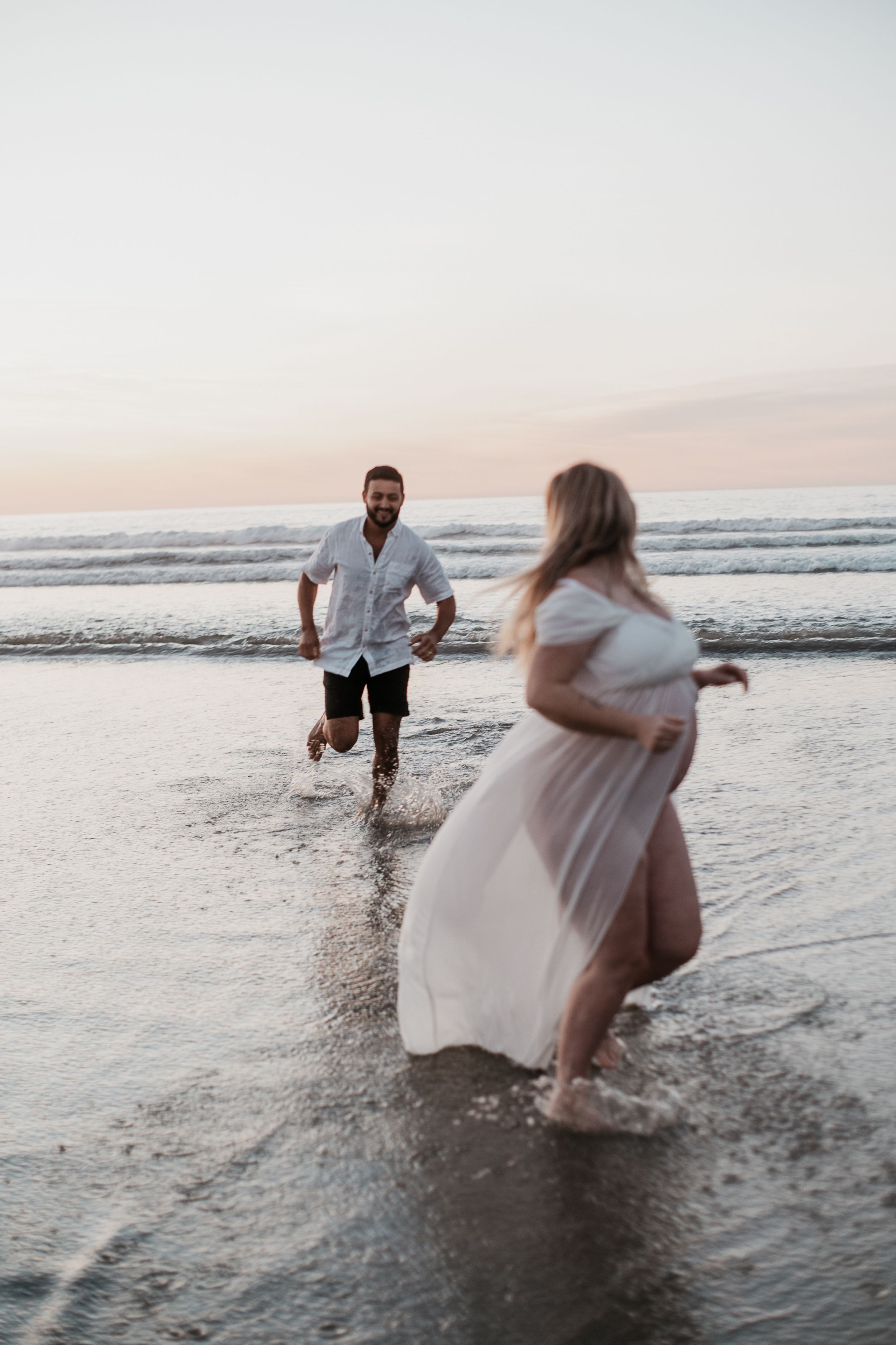 Playful couple running and splashing through ocean waves at golden hour.