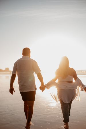 Silhouetted couple walking hand in hand along a beach at golden hour.