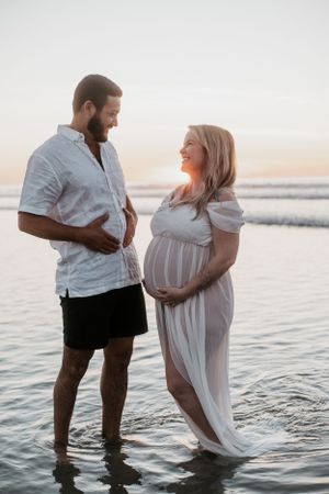 Romantic couple splashing in shallow ocean water during a sunset photoshoot.