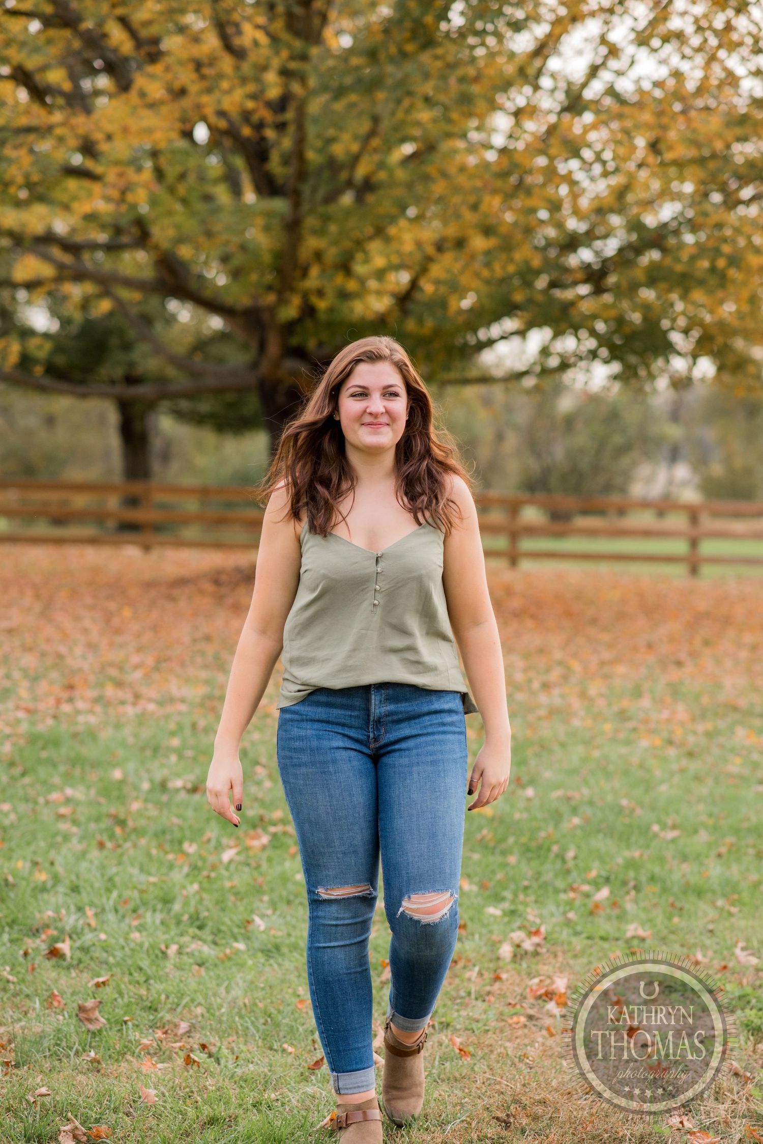 Person in sage tank top and ripped jeans walks through autumn scenery.