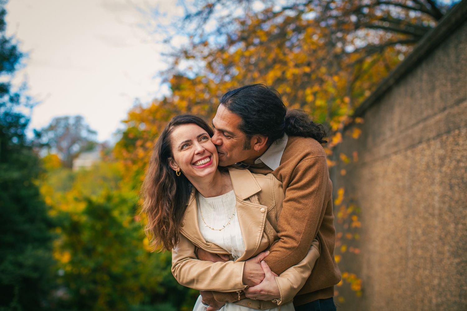 A couple sharing an intimate moment against a backdrop of fall colors and brick wall.