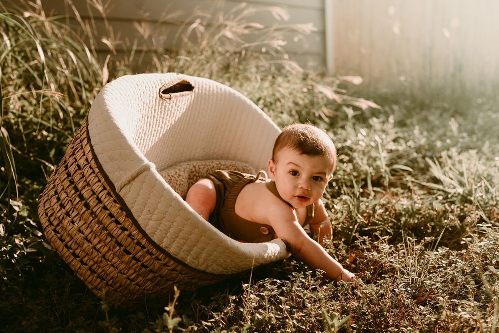 Baby reaching out of white woven basket during outdoor golden hour photoshoot.