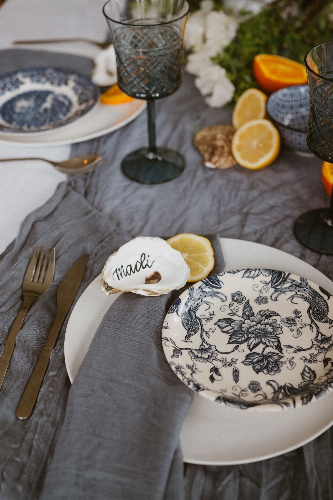 Place setting with blue toile plates, oyster shell place card, and citrus accents.