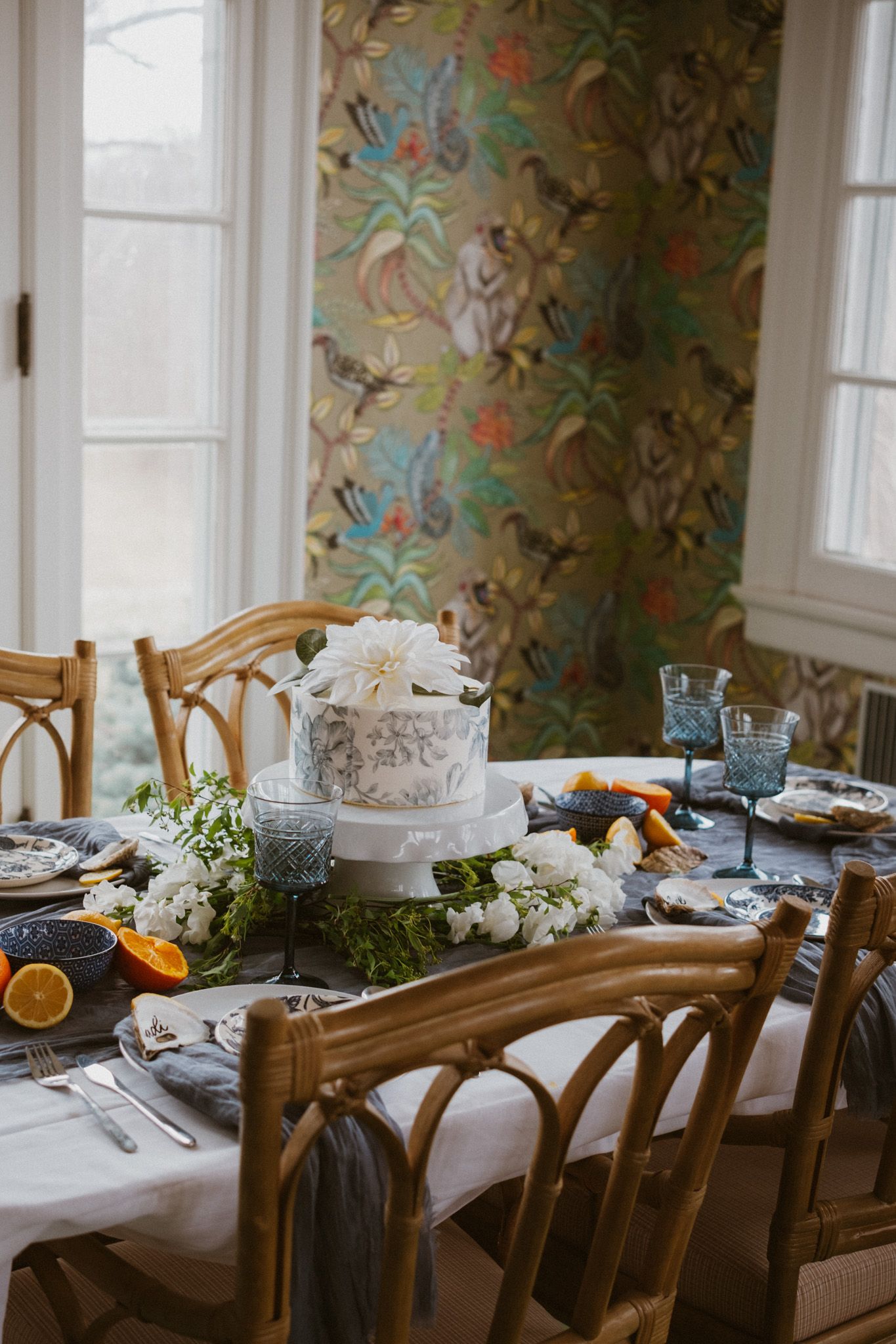 Long dining table set with vintage chairs and floral wallpaper in an elegant room.